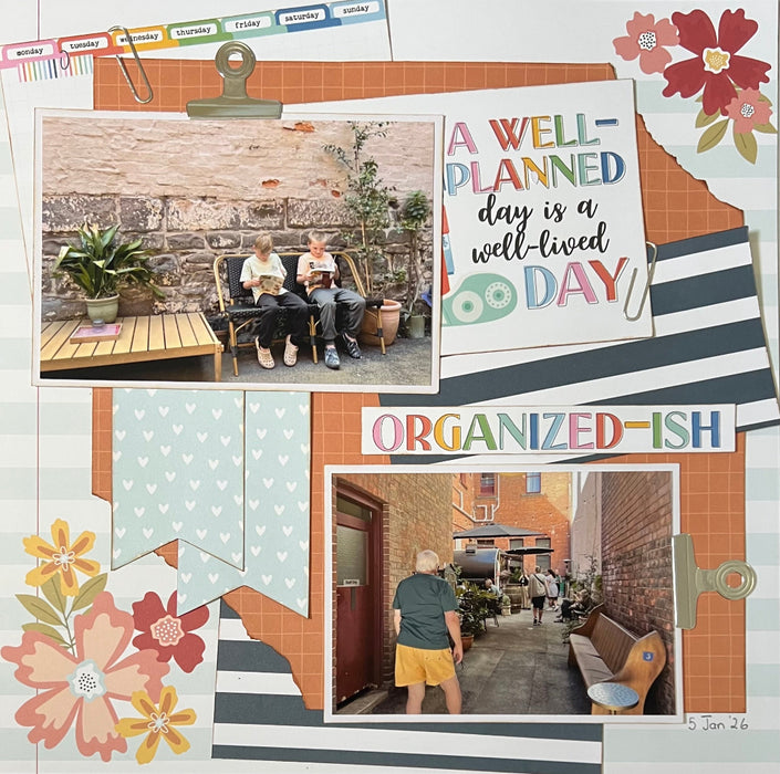 Completed Echo Park Bookish double page scrapbook layout featuring orange grid patterned paper, floral die-cuts, banner embellishments, and journaling cards with "A Well-Planned Day" and "Organized-ish" titles.